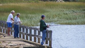 A wooden pier extending into a body of water, with people fishing.