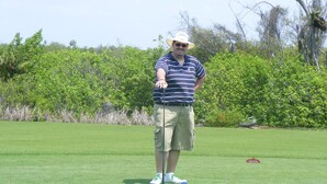 A person standing on a golf course with a putting green and a flagstick.