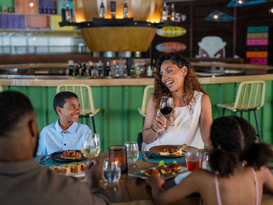 Un restaurante con zona de bar, paredes verdes y una barra con diversas botellas.
