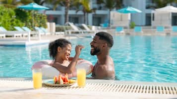 A couple in a swimming pool with a table of food and drinks.