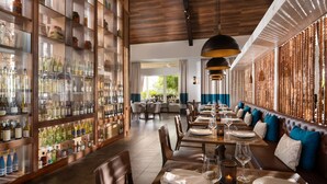 A restaurant with a long dining area, wooden tables, and a bar with glass-fronted shelves of bottles.