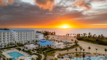 Una località turistica con diverse piscine, una spiaggia e vista sul tramonto sull'oceano.