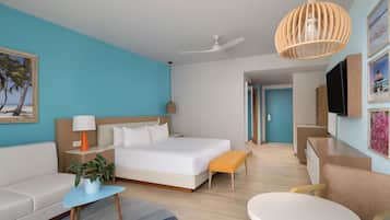 Ett hotellrum med en säng, en soffa, ett litet bord, en bänk, en tv och en takfläkt.