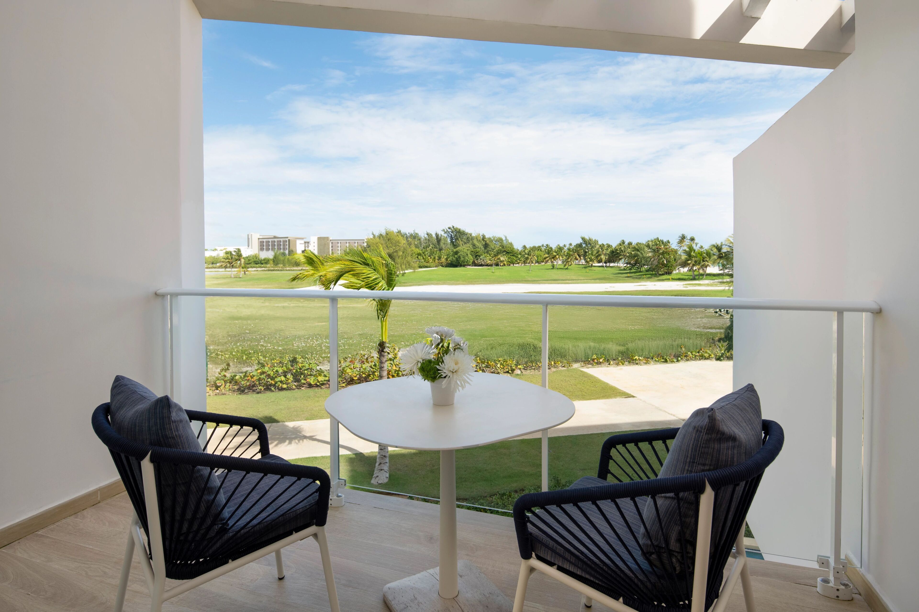 A balcony with two chairs, a small table, and a view of a golf course.
