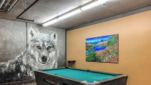 Une table de billard dans une pièce ornée d’une fresque représentant un loup et d’un tableau de paysage au mur.