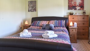 Uma cama bem arrumada com roupa de cama estampada, uma mesa de cabeceira com abajur aquecido, um penteado de madeira e duas pinturas penduradas na parede.