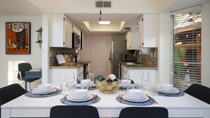 Uma sala de jantar com uma mesa branca posta para quatro pessoas, uma cozinha ao fundo e um cartaz de um cowboy na parede.