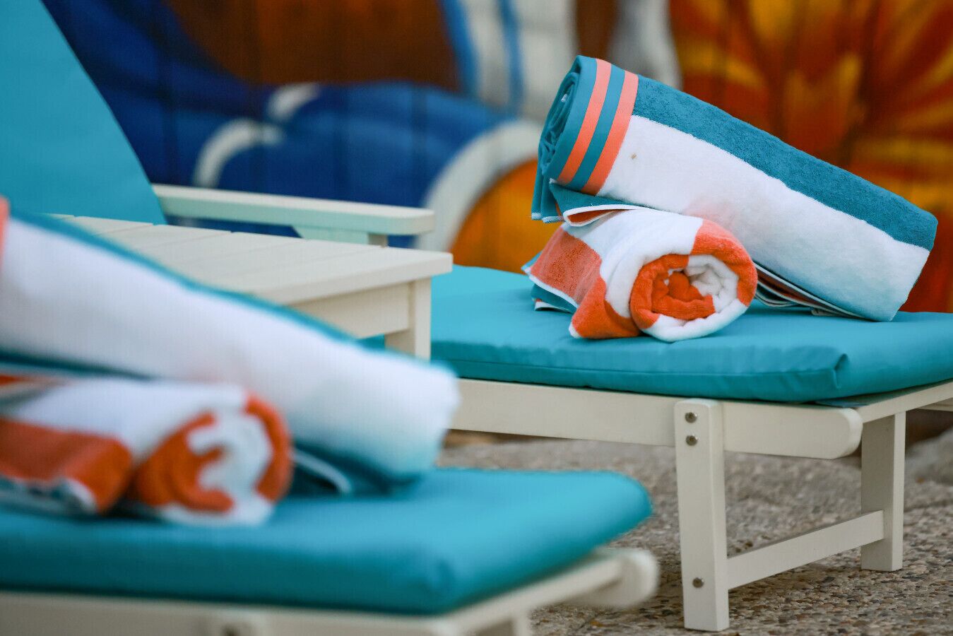 A sun lounger with a teal cushion and a rolled towel with orange and white stripes.