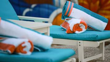 A sun lounger with a teal cushion and a rolled towel with orange and white stripes.