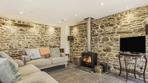 A cozy living room with a stone wall, a sofa, a television, and a wood-burning stove.