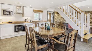A kitchen with white cabinets, a wooden dining table, and a stone staircase.