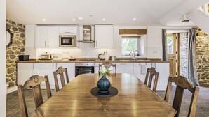 A modern kitchen with white cabinets, a wooden dining table, and a stone accent wall.