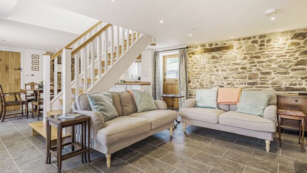 A spacious living area with a stone wall, a wooden staircase, and a sofa with multiple cushions.