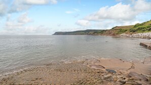 A coastal scene with a paved walkway leading to the water, a rocky shoreline, and a distant cliff. - The Shepherd's Rest (Whitby)