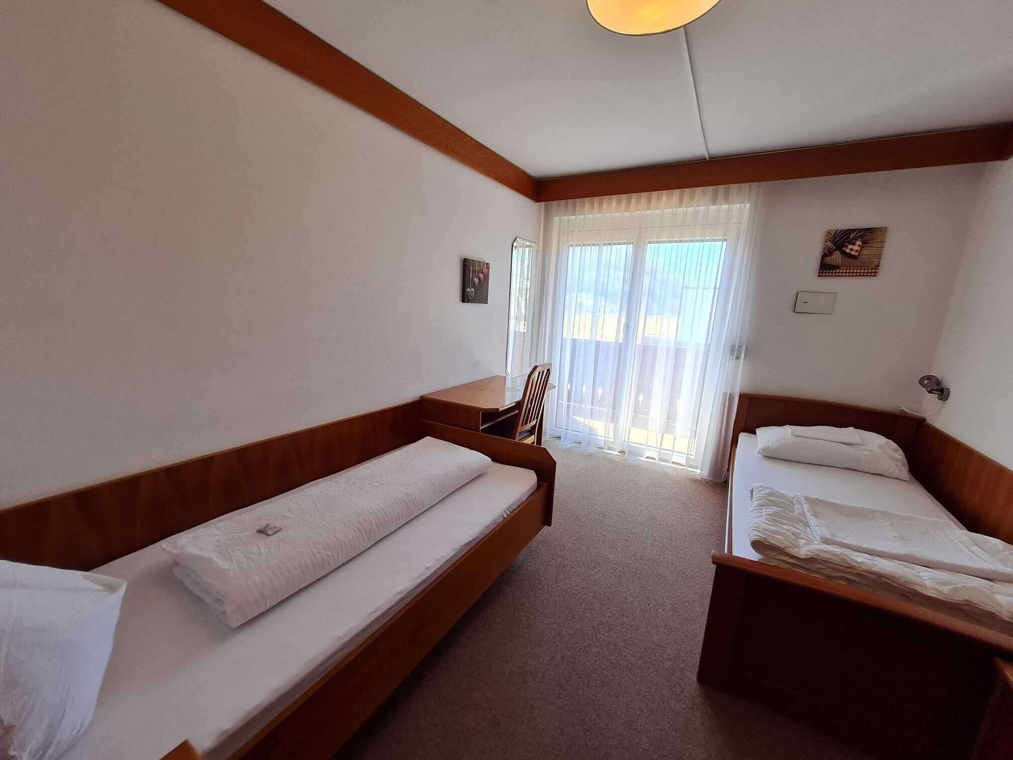 A hotel room with two single beds, a wooden bench, a small table, and a chair.