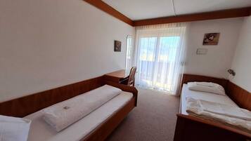 A hotel room with two single beds, a wooden bench, a small table, and a chair.