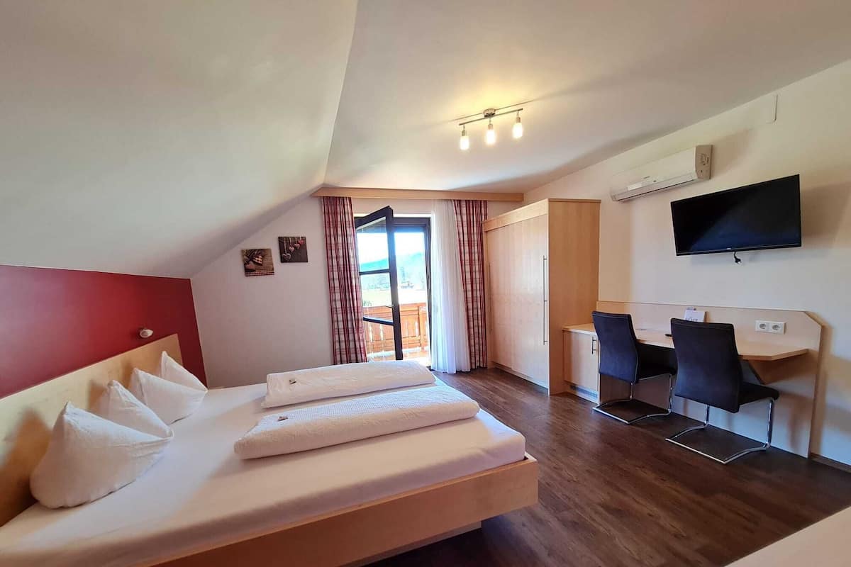 A hotel room with a bed, a desk, a chair, a TV, and a window with curtains.