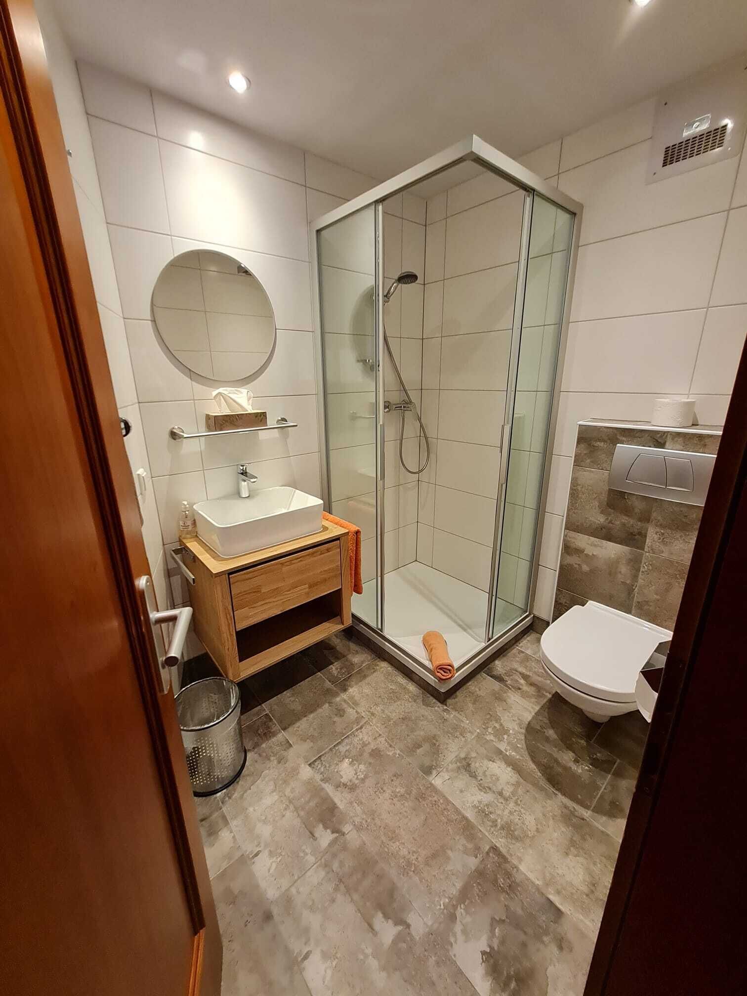 A modern bathroom with a glass-enclosed shower, a wooden vanity, and a white toilet.