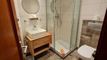 A modern bathroom with a glass-enclosed shower, a wooden vanity, and a white toilet.