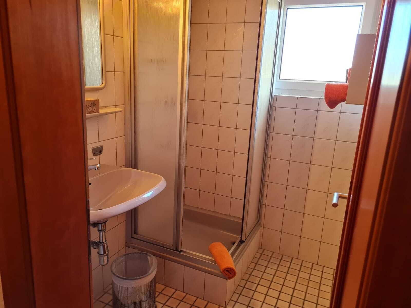 A small bathroom with a shower, a sink, and a window.
