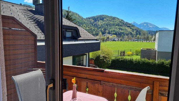 Ein Balkon mit Tisch und Stühlen, mit Blick auf ein grünes Feld und Berge.