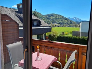 Ein Balkon mit Tisch und Stühlen, mit Blick auf ein grünes Feld und Berge.