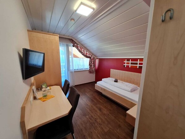 A compact hotel room with a bed, a desk, a chair, a television, and a window with curtains.