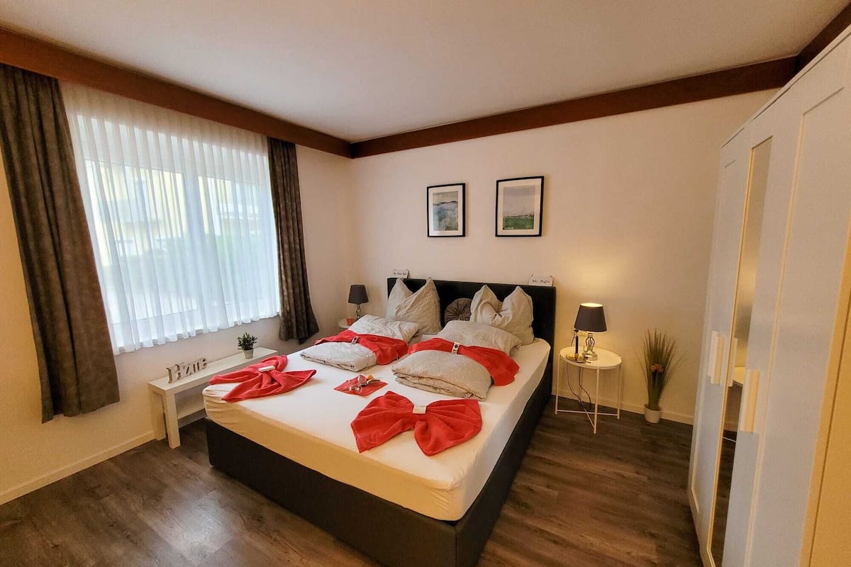 A hotel room with a large bed, two bedside tables, a nightstand, a window with curtains, and a door.