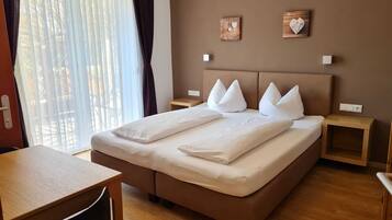 Ein ordentlich eingerichtetes Hotelzimmer mit einem großen Bett, zwei Nachttischen, einem kleinen Holztisch und Blick durch ein Fenster mit transparenten Vorhängen.