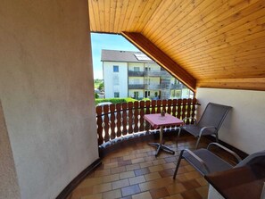A balcony with a wooden ceiling, a table with a checkered tablecloth, and two chairs. - Pension Tulpe (Sankt Kanzian am Klopeiner See)