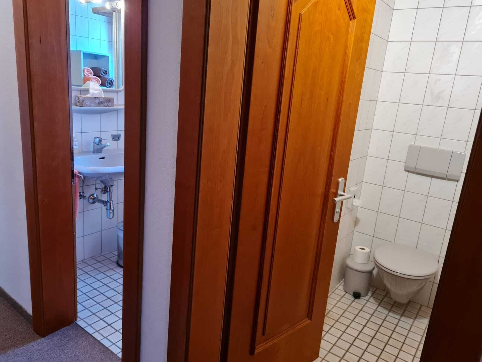 Une salle de bain avec des toilettes blanches, un lavabo et un miroir.
