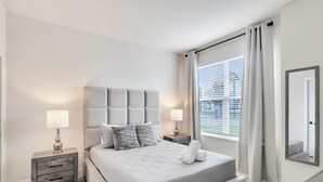Een moderne slaapkamer met een groot bed, twee nachtkastjes met lampen, een raam met zonwering en een spiegel aan de muur.