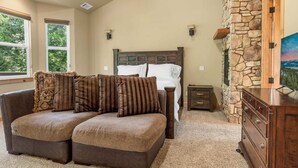Un dormitorio con una cama grande, una chimenea de piedra, un aparador de madera y un sofá para dos personas.