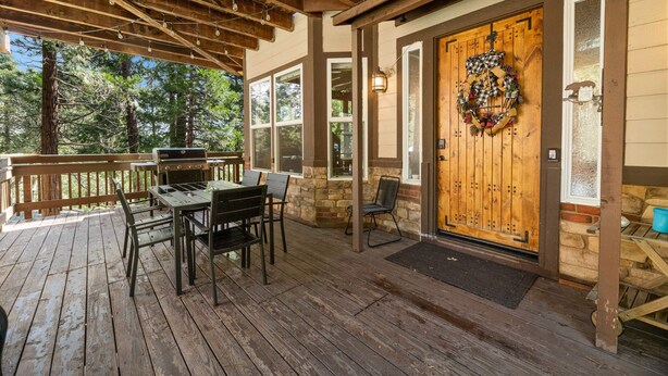 Una terraza cubierta al aire libre con una mesa y sillas de madera, un muro de piedra y una puerta de madera con un adorno.