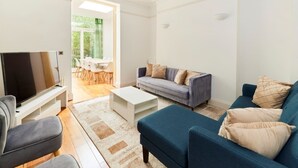 A modern living room with a grey sofa, a blue sofa, a white coffee table, and a flat-screen TV. - The Woolwich Retreat - Enticing 5bdr House With Parking (London)