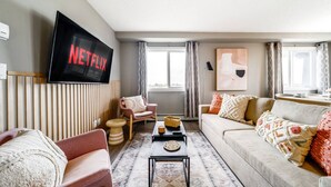 A living room with a flat-screen TV, a sofa, a chair, a coffee table, and a patterned rug.
