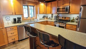 A modern kitchen with wooden cabinets, stainless steel appliances, and a bar area with stools. - Goat Wall Cabin: log cabin retreat on the meadow (Mazama)