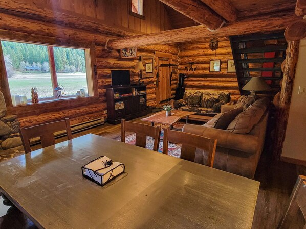 Interior rústico con una mesa de comedor de madera, un sofá, un televisor y una estantería.