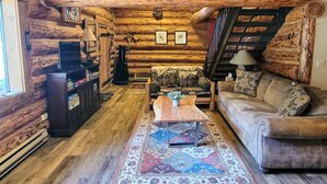 A log cabin interior with a sofa, coffee table, fireplace, and a staircase. - Goat Wall Cabin: log cabin retreat on the meadow (Mazama)