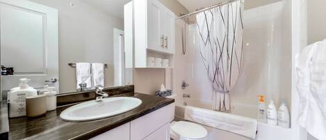 A modern bathroom with a white sink, vanity, and toilet. There are toiletries on the counter and a shower curtain with a tree design.