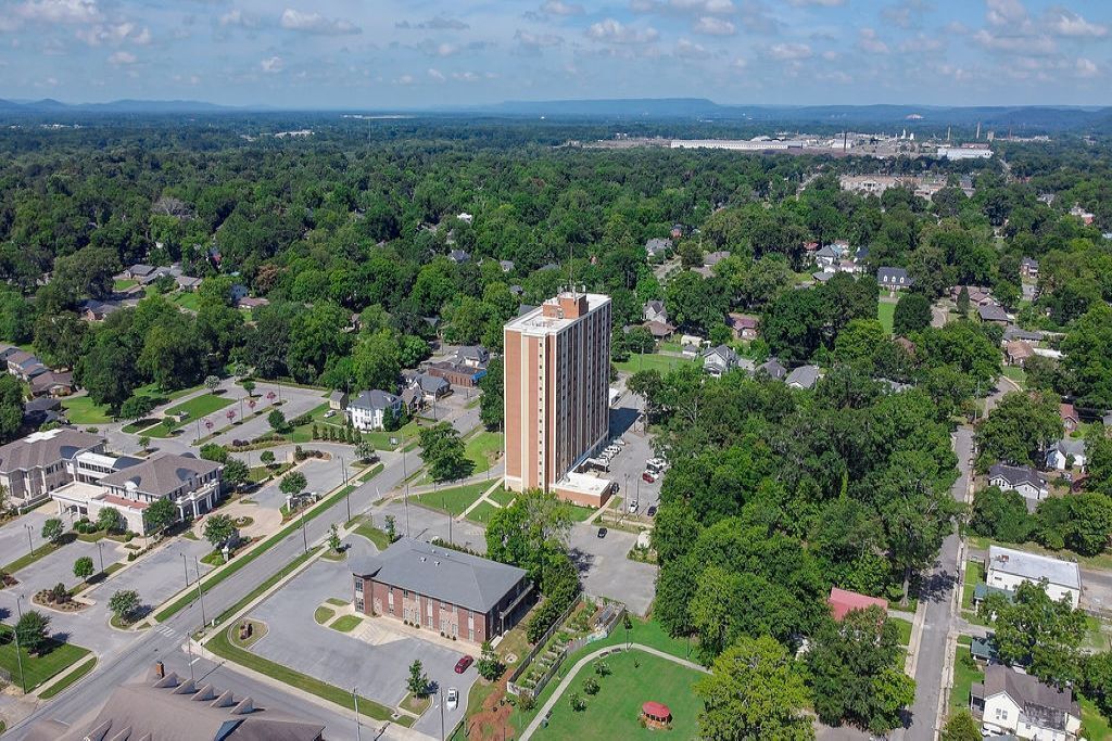 An aerial view of a residential area with a prominent tall building, surrounded by houses and greenery.
