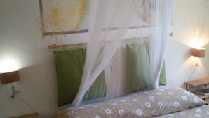 A bedroom with a bed covered by a mosquito net, two bedside tables with lamps, and a wall with a floral painting.