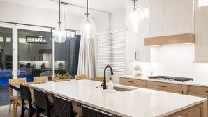 A modern kitchen with a large island, pendant lighting, and a view of the outdoor area. - The Gambit Luxury Zion Home Pool Hot Tub Sleeps 14 (Hurricane)