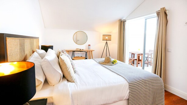 A neatly arranged bedroom with a bed, bedside lamp, and a small table with a lamp. - Young Spirit Apartment (Faro)