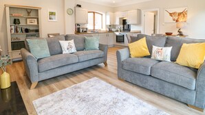 A modern living room with two grey sofas, a white rug, and a kitchen in the background. - Avenue Croft (Nottingham)