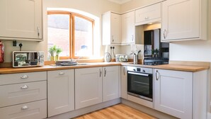 A modern kitchen with light-colored cabinets, a wooden countertop, a built-in oven, and a window providing natural light. - Avenue Croft (Nottingham)