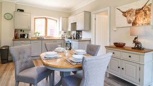 A modern kitchen with a dining area, featuring a round wooden table, grey upholstered chairs, and a white cabinet with a decorative animal head. - Avenue Croft (Nottingham)