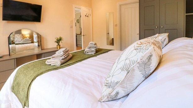 A hotel room with a bed, a TV mounted on the wall, a mirror, a wardrobe, and a small plant. - Avenue Croft (Nottingham)