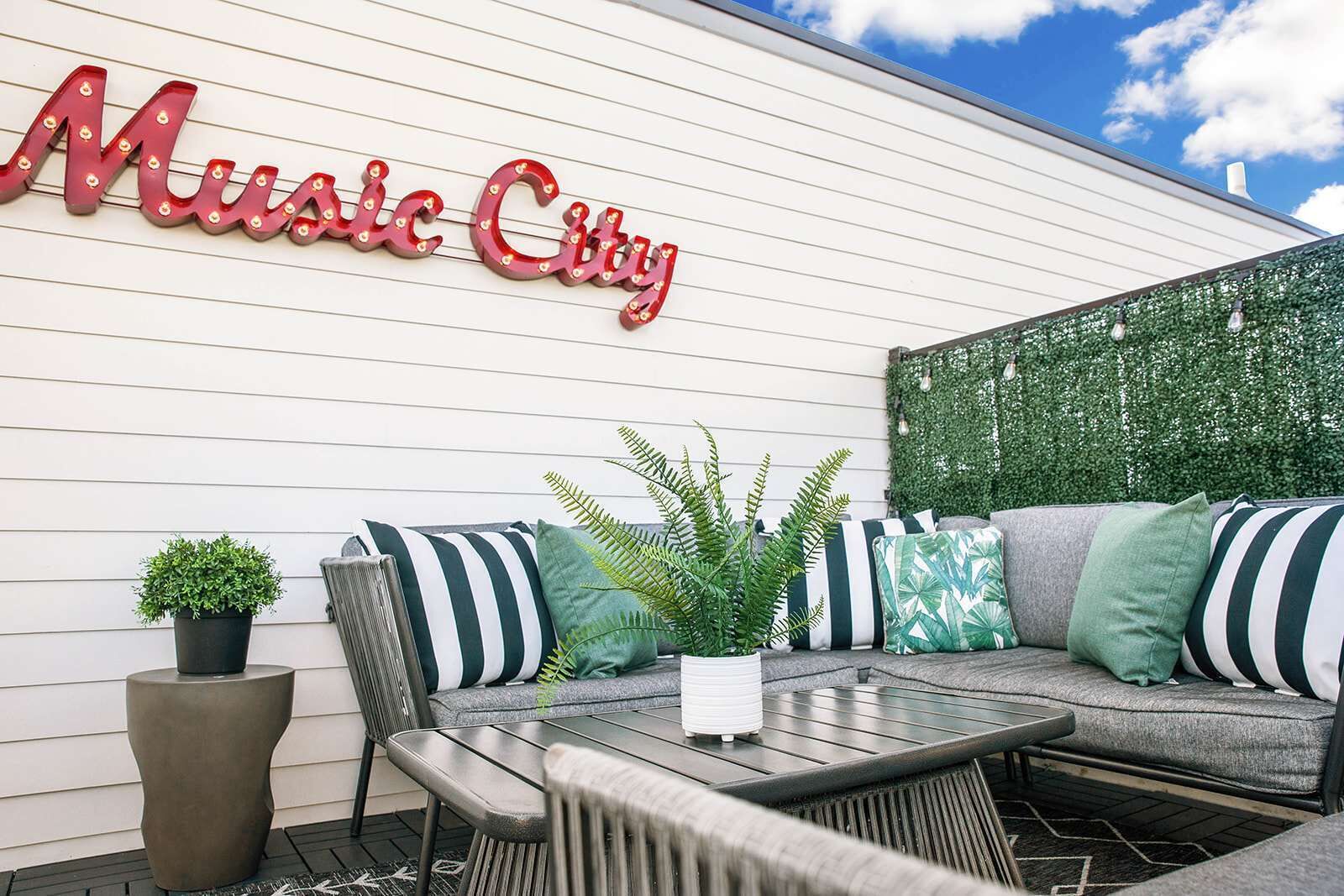 An outdoor seating area with a sofa, chairs, and a table. A sign reading "Music City" is visible on the wall.