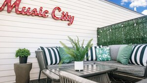 Un área de estar al aire libre con un sofá, sillas y una mesa. Se ve un letrero en la pared que dice "Music City".
